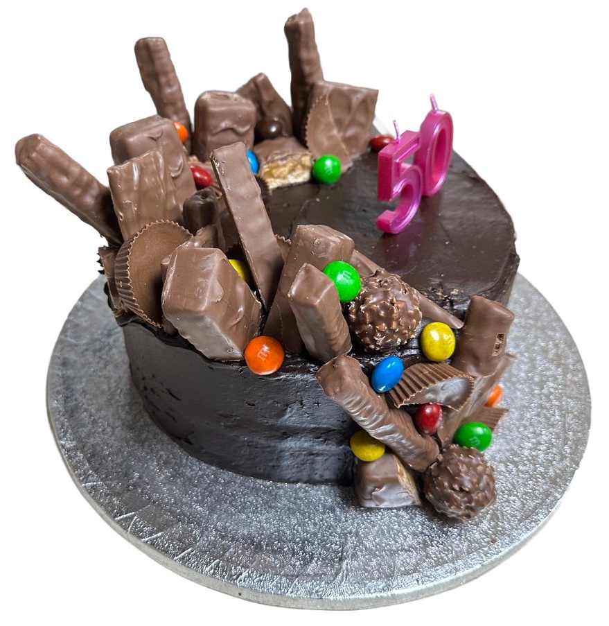 A dark chocolate celebration cake crowded with chocolate bars, peanut butter cups, malt balls, candy-coated chocolates, and pink number 50 candles.