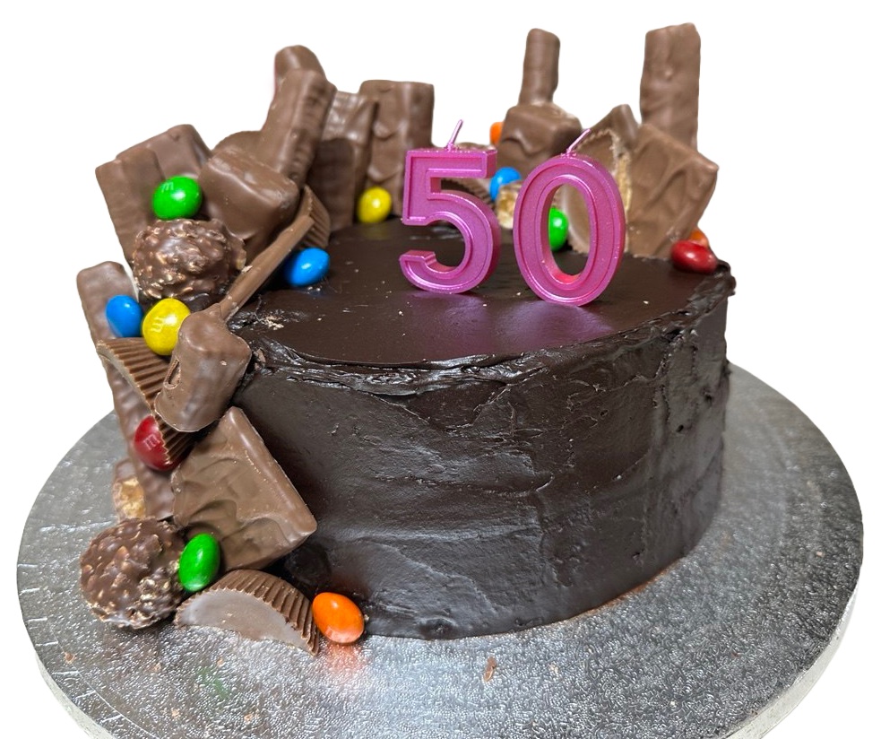 Chocolate celebration cake with pink number 50 candles and chocolate bars, sweets, and a malt ball along one side.