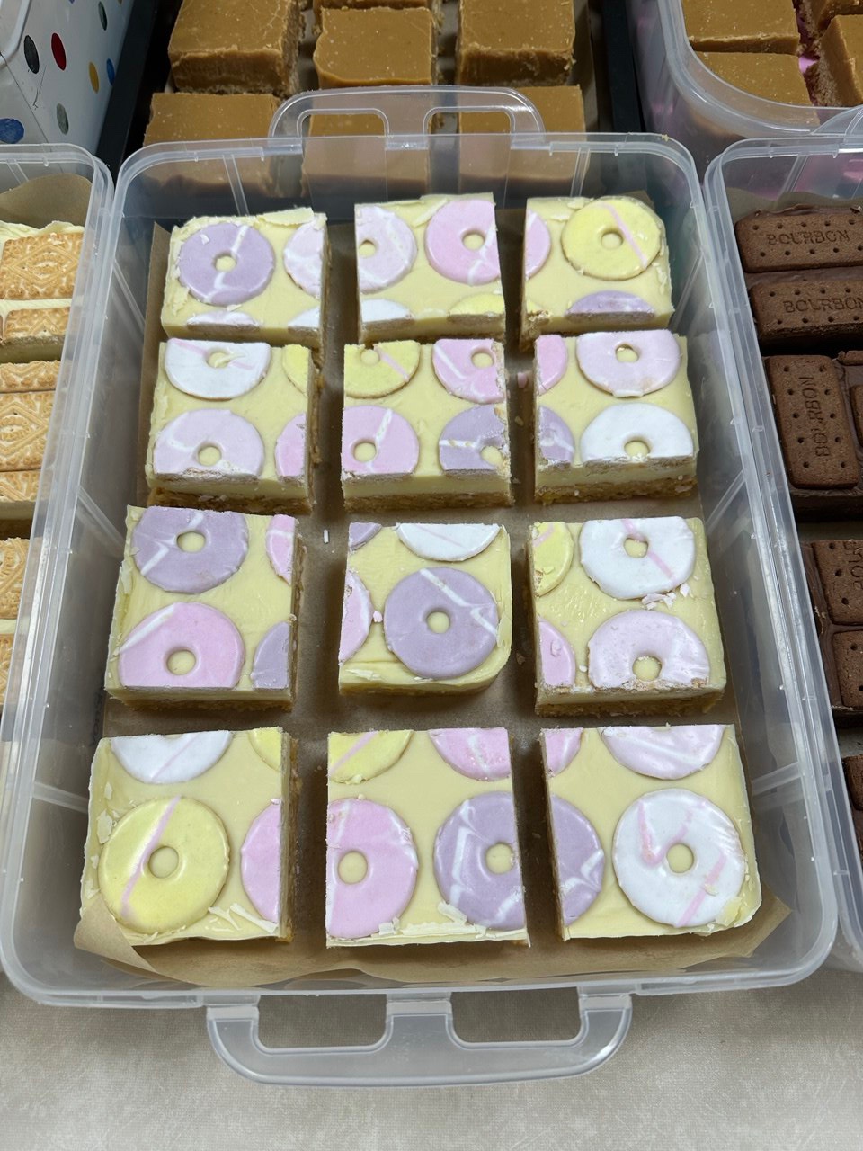 A tub of pale yellow squares topped with pink, lilac, and white ring sweets.